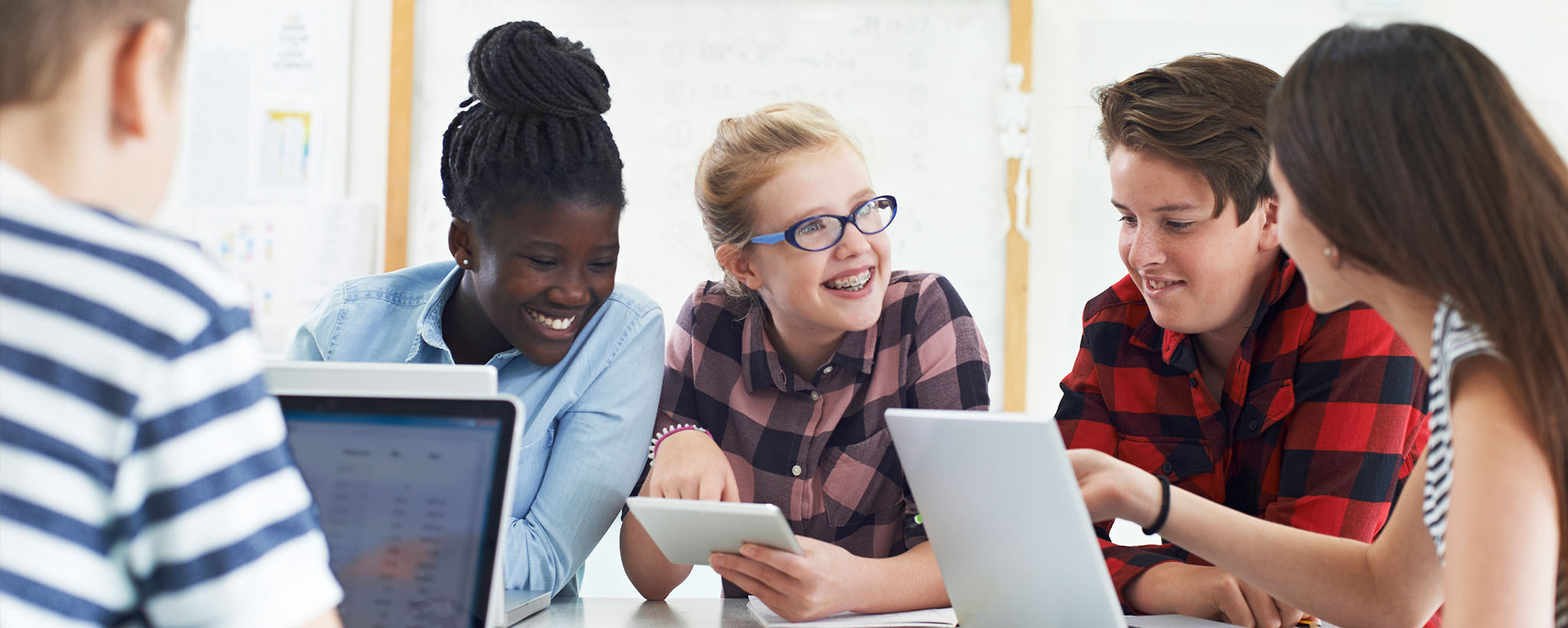 Teens sitting around a table talking and looking at laptops